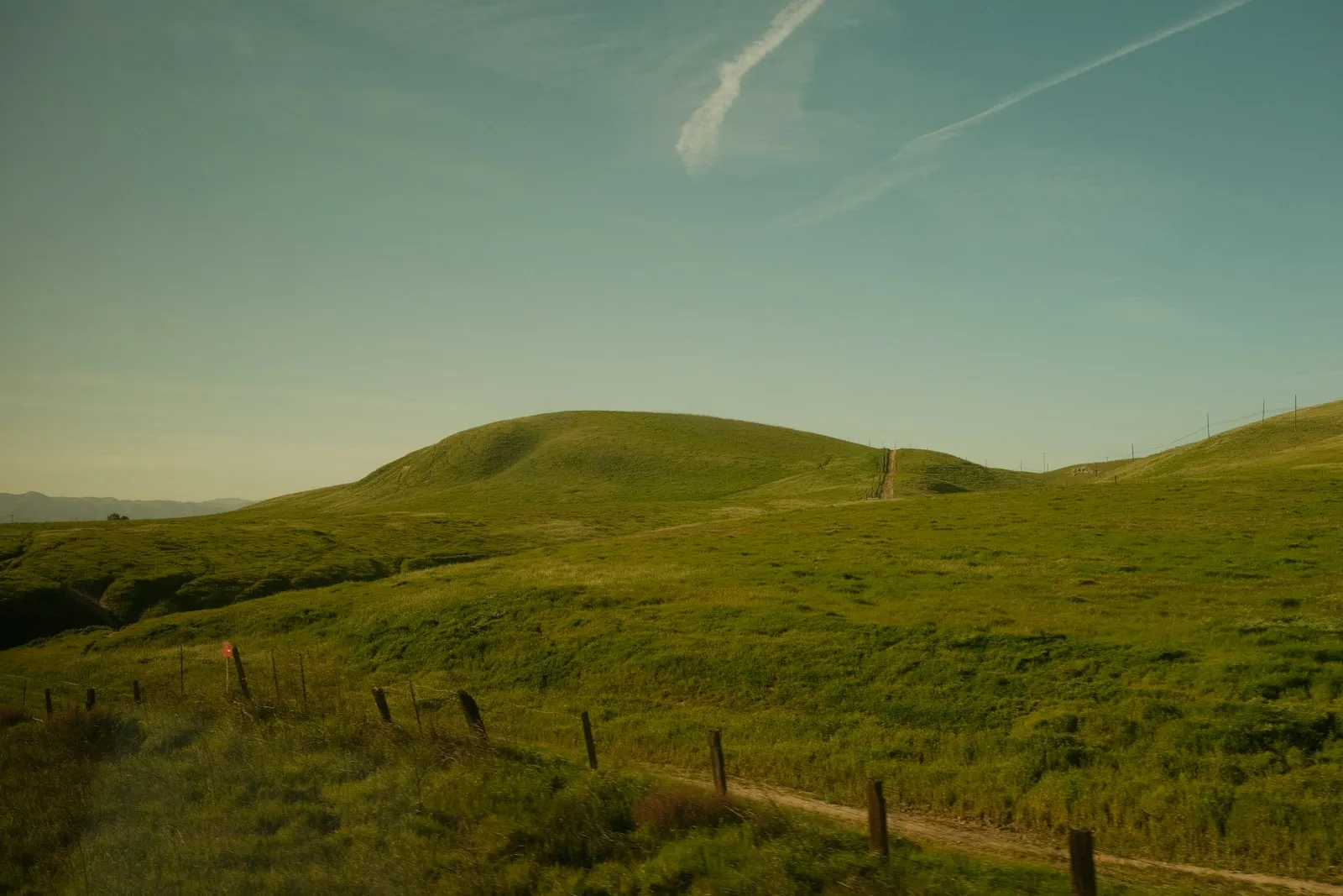 A dirt road winding through green hillside A dirt road winding through green hillside